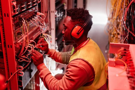 Photo for Side view portrait of technician setting up network in server room and wearing ear protection lit by red neon lights - Royalty Free Image