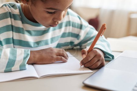 Téléchargez les photos : Gros plan de fille noire écrivant dans un carnet tout en faisant des devoirs au bureau, espace de copie - en image libre de droit