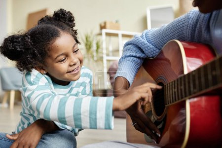 Photo for Close up of cute black girl enjoying music lesson at home and playing with guitar strings - Royalty Free Image