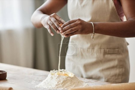 Foto de Primer plano de la mujer negra horneando en la cocina y rompiendo huevos y mezclando con harina mientras hace masa de pastelería casera, espacio de copia - Imagen libre de derechos