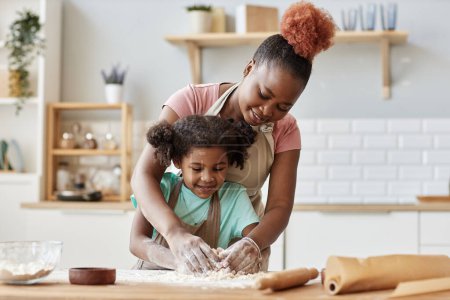 Téléchargez les photos : Portrait de la famille noire aimante mère et fille cuisiner ensemble dans la cuisine confortable maison, espace de copie - en image libre de droit