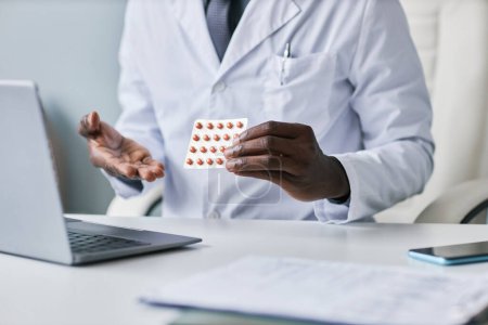Photo for Close up of black doctor holding tablets and explaining medication to client during online consultation - Royalty Free Image