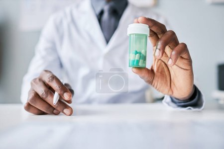 Photo for Close up of black doctor holding bottle of pills to camera while explaining treatment and medication side effects - Royalty Free Image