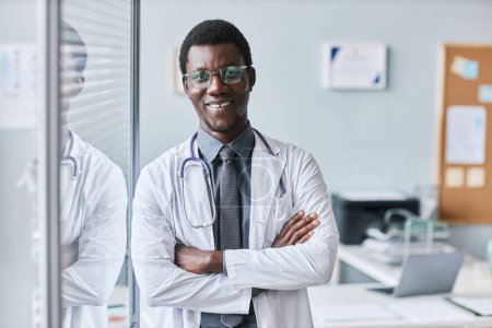 Photo for Waist up portrait of confident black doctor leaning on glass wall in office and smiling at camera, copy space - Royalty Free Image