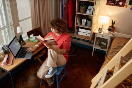 Photo for High angle portrait of curly haired girl studying in college dorm room and reading books, copy space - Royalty Free Image