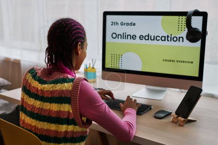 Foto de Vista posterior de la chica adolescente negro utilizando la computadora en casa y navegar por el sitio web de educación en línea - Imagen libre de derechos