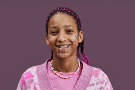 Photo for Close up portrait of black teenage girl with sparkling tattoos on face smiling at camera against pink background - Royalty Free Image
