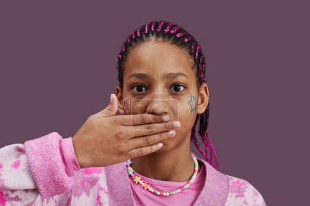 Foto de Retrato mínimo de adolescente negro cerrando la boca y en la cámara contra el fondo rosa - Imagen libre de derechos