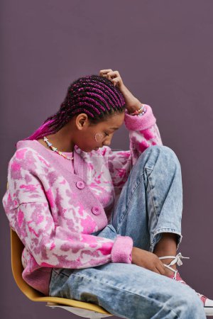 Téléchargez les photos : Vue latérale verticale portrait d'adolescente noire portant des vêtements décontractés à la mode posant assis sur une chaise avec les pieds vers le haut - en image libre de droit