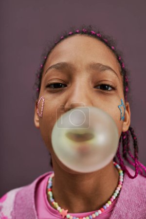 Photo for Vertical fisheye portrait of black teenage girl blowing bubblegum bubble in pink tones - Royalty Free Image
