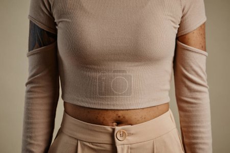 Téléchargez les photos : Gros plan minimal d'une femme méconnaissable portant une chemise de culture de couleur neutre avec des découpes, espace de copie - en image libre de droit