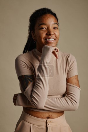 Téléchargez les photos : Portrait vertical taille haute de jeune femme noire souriant sincèrement et regardant la caméra dans des tons neutres - en image libre de droit