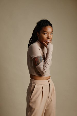 Foto de Retrato vertical de una joven negra con tatuajes posando con confianza sobre fondo beige neutro en el estudio - Imagen libre de derechos