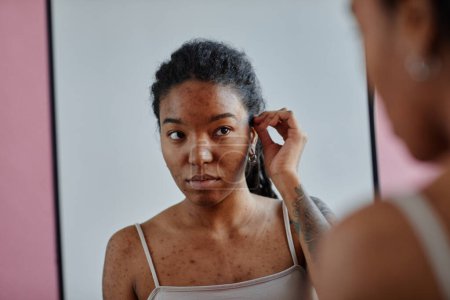 Foto de Retrato de una joven mujer negra con cicatrices de acné mirando en el espejo inseguro en apariencia - Imagen libre de derechos