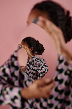 Foto de Retrato gráfico de mujer negra irreconocible sosteniendo espejo con ilusión óptica, concepto de autorreflexión - Imagen libre de derechos