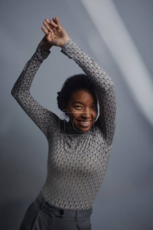 Foto de Retrato mínimo de mujer negra sonriente mirando a la cámara y bailando sobre fondo gris acero - Imagen libre de derechos