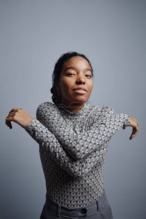 Photo for Vertical portrait of young black woman dancing against steel gray background and looking at camera, minimal - Royalty Free Image