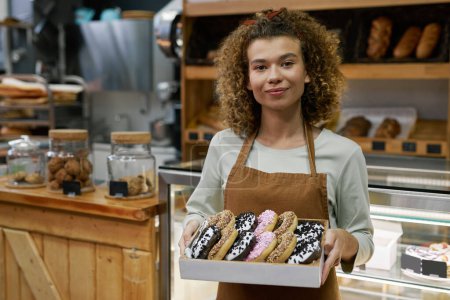 Photo for Positive baker holding box of delicious glazed donuts of different colors - Royalty Free Image