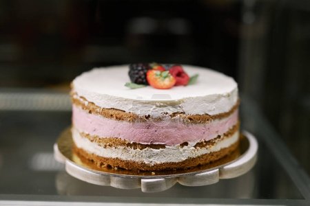 Foto de Delicioso pastel con glaseado rosa y blanco decorado con bayas frescas en escaparate de panadería - Imagen libre de derechos