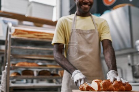 Téléchargez les photos : Sourire boulanger coupe de pain tressé avec des graines de pavot pour le client - en image libre de droit