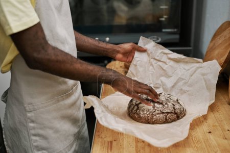 Téléchargez les photos : Mains de pain de seigle enveloppant boulanger sur papier pour le client - en image libre de droit