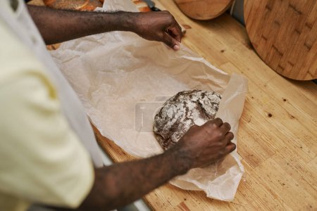Photo for Hands of bakery worker wrapping loaf of rye bread in paper - Royalty Free Image
