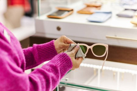 Foto de Primer plano del asistente de ventas limpiando gafas de sol de moda en una boutique de lujo, espacio para copiar - Imagen libre de derechos