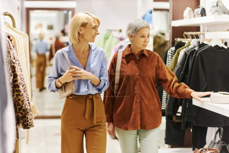Téléchargez les photos : Portrait de la femme adulte souriante avec sa mère faisant du shopping ensemble dans une boutique de vêtements et marchant vers la caméra - en image libre de droit