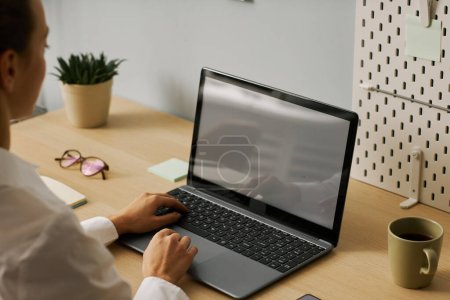 Téléchargez les photos : Gros plan de la jeune femme tapant à l'ordinateur portable avec écran blanc tout en travaillant dans le bureau, espace de copie - en image libre de droit