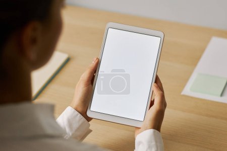Foto de Primer plano mínimo de una mujer joven sosteniendo una tableta digital con una maqueta de pantalla blanca en el lugar de trabajo - Imagen libre de derechos