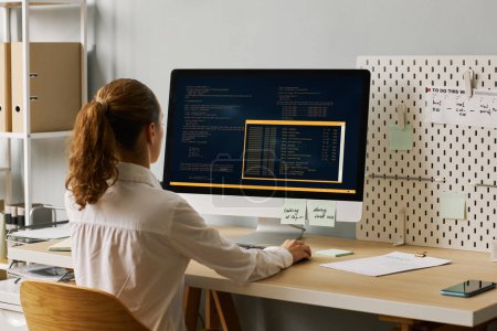 Photo for Back view of female programmer writing code while working at desk, copy space - Royalty Free Image