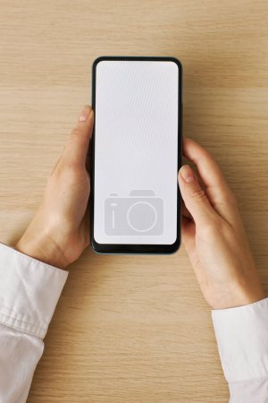 Photo for Top view closeup of woman holding smartphone with white screen mockup over light wood desk - Royalty Free Image