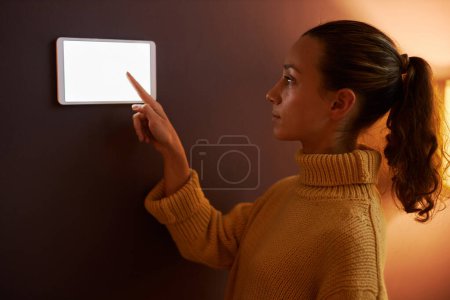 Téléchargez les photos : Portrait latéral de jeune femme utilisant le panneau de commande numérique sur le mur à la maison - en image libre de droit