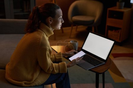 Téléchargez les photos : Portrait latéral de jeune femme utilisant des appareils avec des maquettes d'écran blanc dans un cadre de détente à la maison - en image libre de droit
