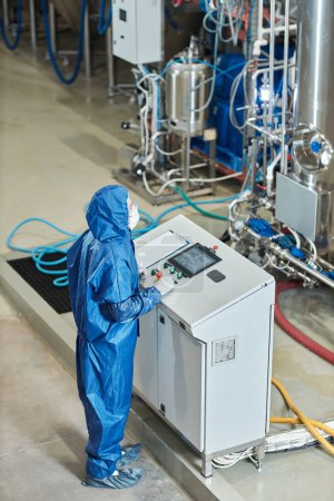 Téléchargez les photos : Portrait vertical du travailleur en équipement de protection opérant à l'usine debout près du panneau de commande - en image libre de droit