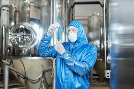 Foto de Retrato de cintura hacia arriba del trabajador que usa equipo de protección y sostiene el tubo de ensayo en la planta química - Imagen libre de derechos