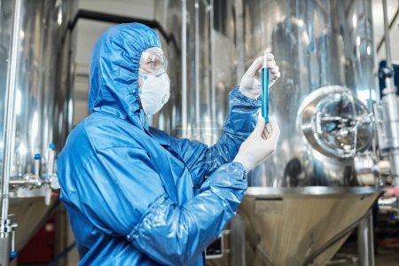 Photo for Side view portrait of worker wearing protective gear and holding test tube at chemical plant - Royalty Free Image