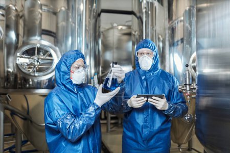 Photo for Waist up portrait of two workers doing tests at chemical factory and wearing protective suits - Royalty Free Image