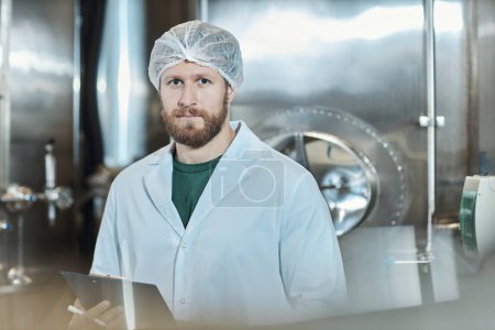 Téléchargez les photos : Portrait à la taille d'un ouvrier portant un manteau de laboratoire debout à un atelier d'usine alimentaire et tenant un presse-papiers, espace de copie - en image libre de droit