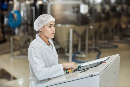Photo for Side view portrait of female worker wearing lab coat using control panel at food factory, copy space - Royalty Free Image
