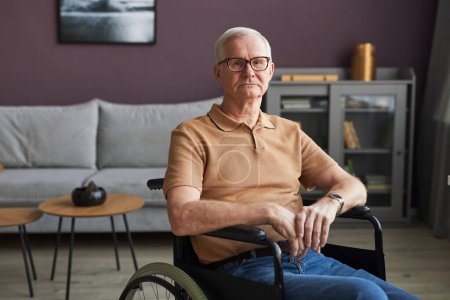 Photo for Portrait of senior man with disability sitting on wheelchair in the living room and looking at camera - Royalty Free Image