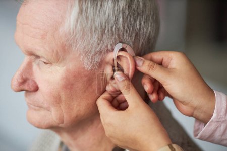 Foto de Primer plano del trabajador social que ayuda a usar audífonos en la oreja del hombre mayor sordo - Imagen libre de derechos