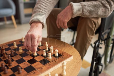 Foto de Primer plano del hombre mayor con discapacidad sentado en silla de ruedas y jugando al ajedrez en la mesa - Imagen libre de derechos