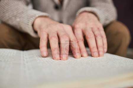 Foto de Primer plano del hombre mayor con discapacidad visual que usa sus manos para leer el libro en Braille en la mesa - Imagen libre de derechos