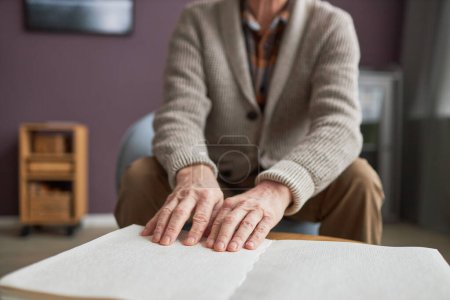 Téléchargez les photos : Gros plan d'un aîné handicapé lisant un livre en braille à table pendant ses loisirs à la maison - en image libre de droit