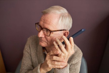 Photo for Blind man with gray hair in eyeglasses listening to audio on his mobile phone - Royalty Free Image