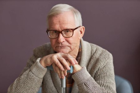 Téléchargez les photos : Portrait d'homme âgé aux cheveux gris dans des lunettes assis sur un fauteuil avec un bâton et regardant la caméra - en image libre de droit