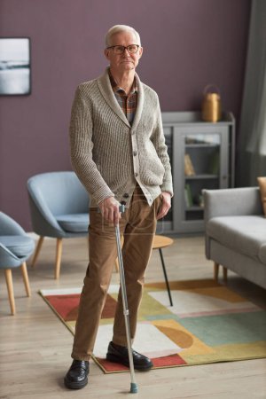 Photo for Portrait of serious senior man in eyeglasses standing with stick in the modern living room - Royalty Free Image