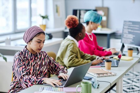 Photo for Diverse group of creative young people sitting in row while working in office focus on Muslim woman using laptop in foreground - Royalty Free Image