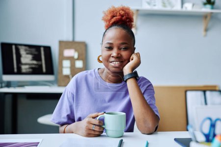 Foto de Retrato de vista frontal de una joven negra vestida de púrpura en el lugar de trabajo y sonriendo a la cámara - Imagen libre de derechos